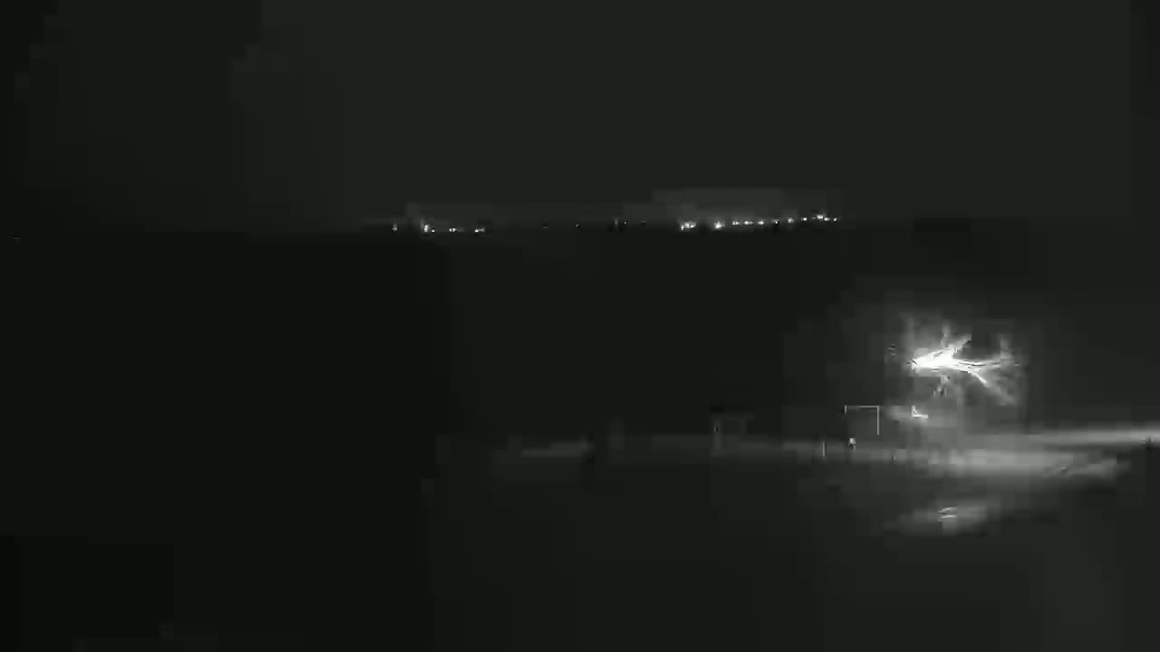 A nighttime outdoor scene shows a lightning strike in the foreground with distant city lights visible on the horizon under a dark sky.