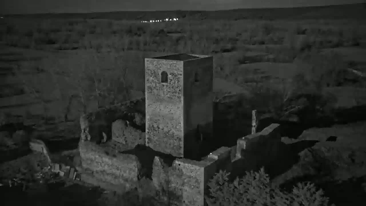 An aerial nighttime view shows the stone ruins of a building, including a standing tower, under a dark sky.