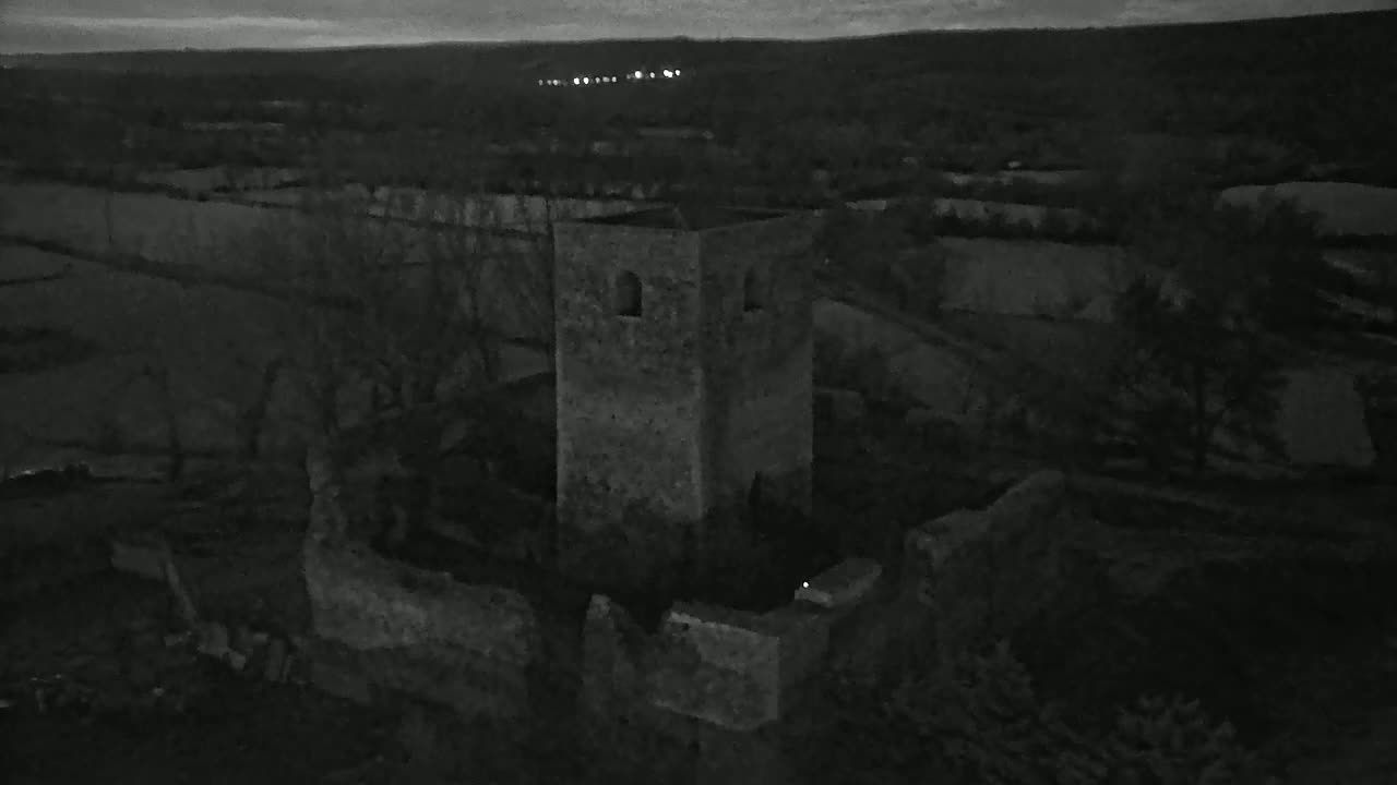An aerial, nighttime view shows the ruins of a stone tower and surrounding structures under a dark sky.