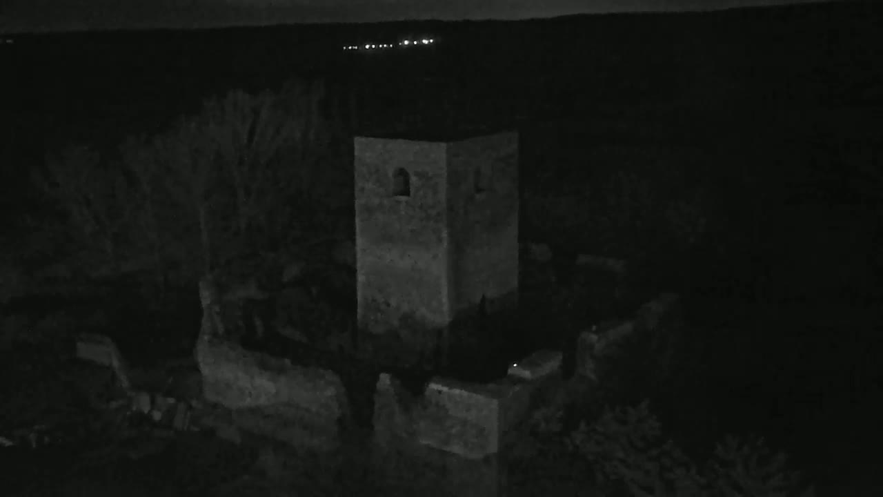 A stone tower, part of a larger ruined structure, is seen at night under a dark sky with a few distant lights visible on the horizon.