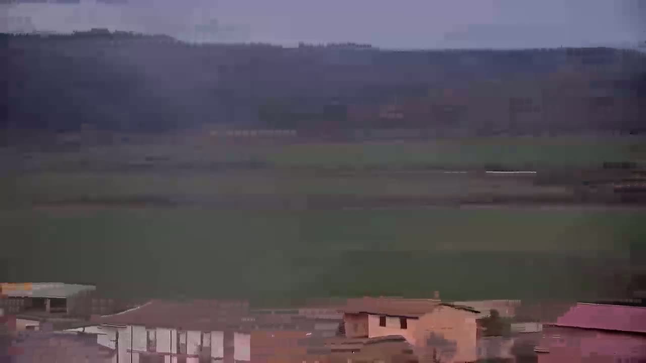A hazy, overcast day reveals a flat expanse of green fields extending to a distant line of dark hills, with a small collection of buildings in the foreground.