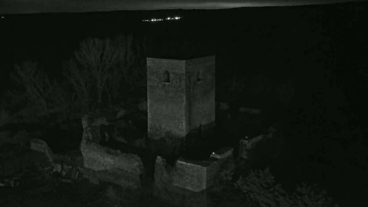 A stone tower, part of a larger ruined structure, stands under a dark night sky with distant lights visible on the horizon.
