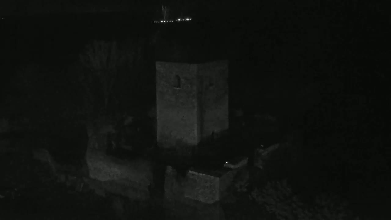 A stone tower is dimly lit at night, surrounded by dark vegetation and a low wall.