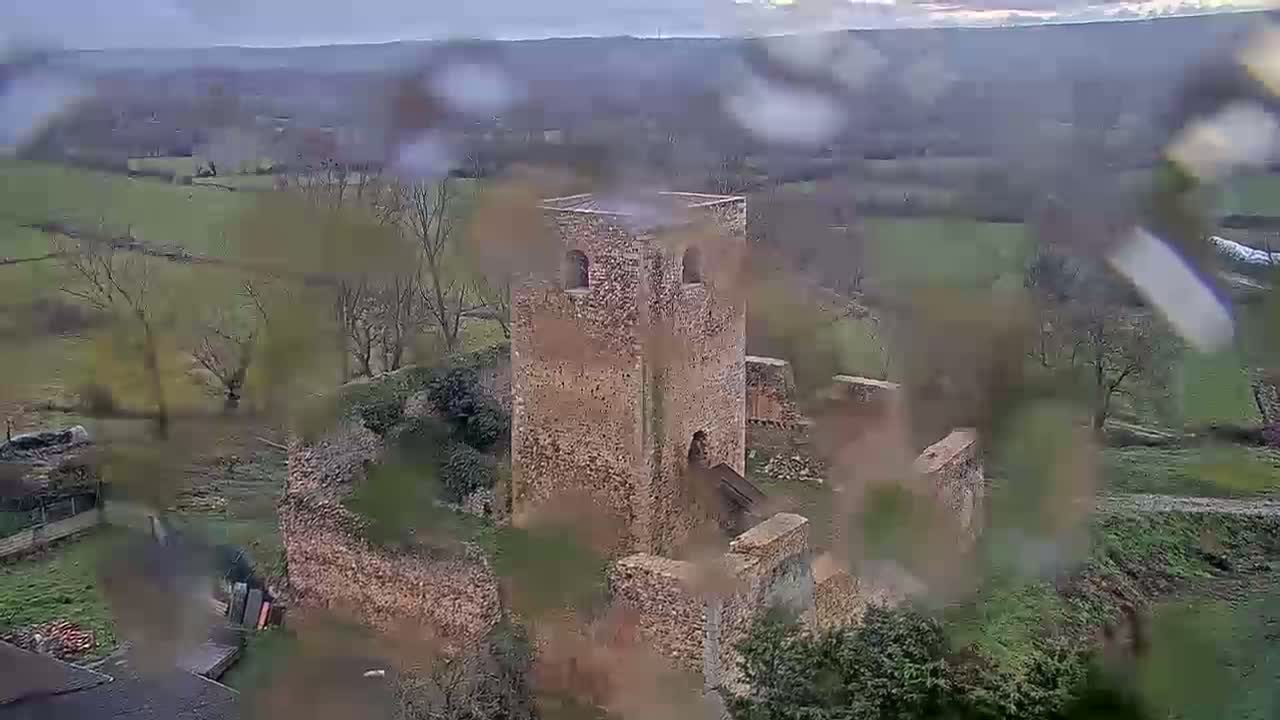 Rain falls on a stone tower and surrounding ruins nestled in a hilly, green landscape.