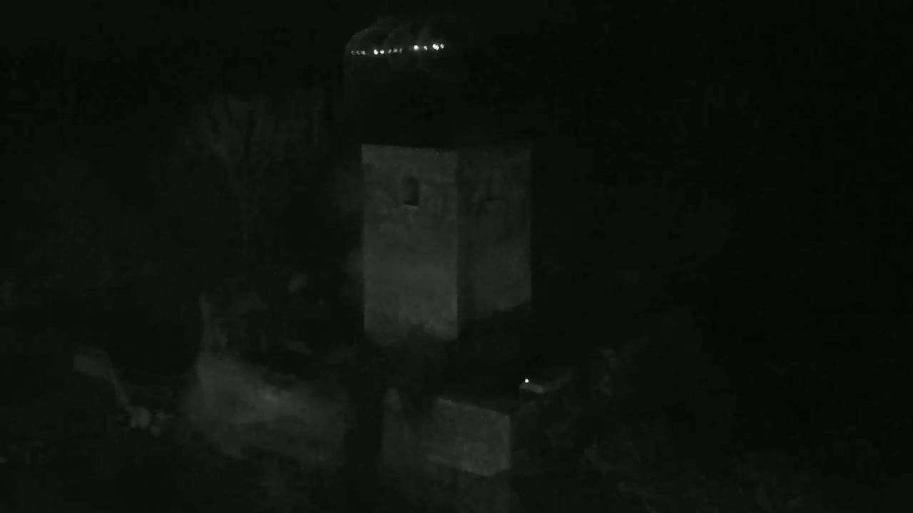 A low-light image shows a stone tower at night, with a few faint lights visible in the distance.