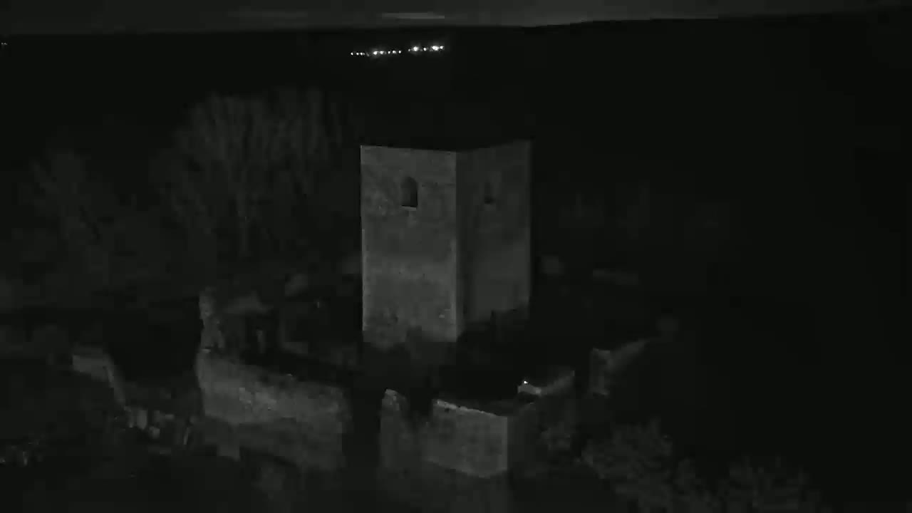 A stone tower, part of a larger stone structure, stands in darkness under a clear night sky.