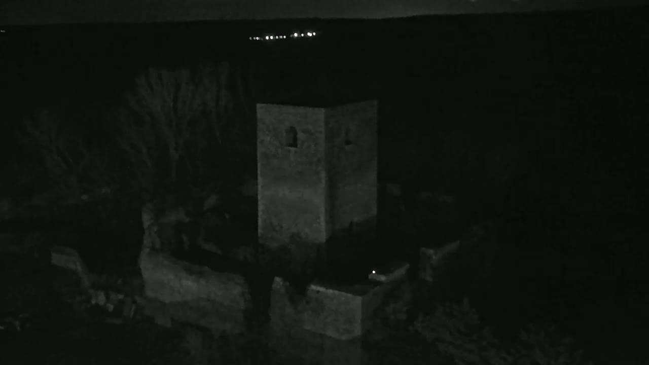 A square stone tower stands in the darkness of night, with a faint glow visible in the distance.