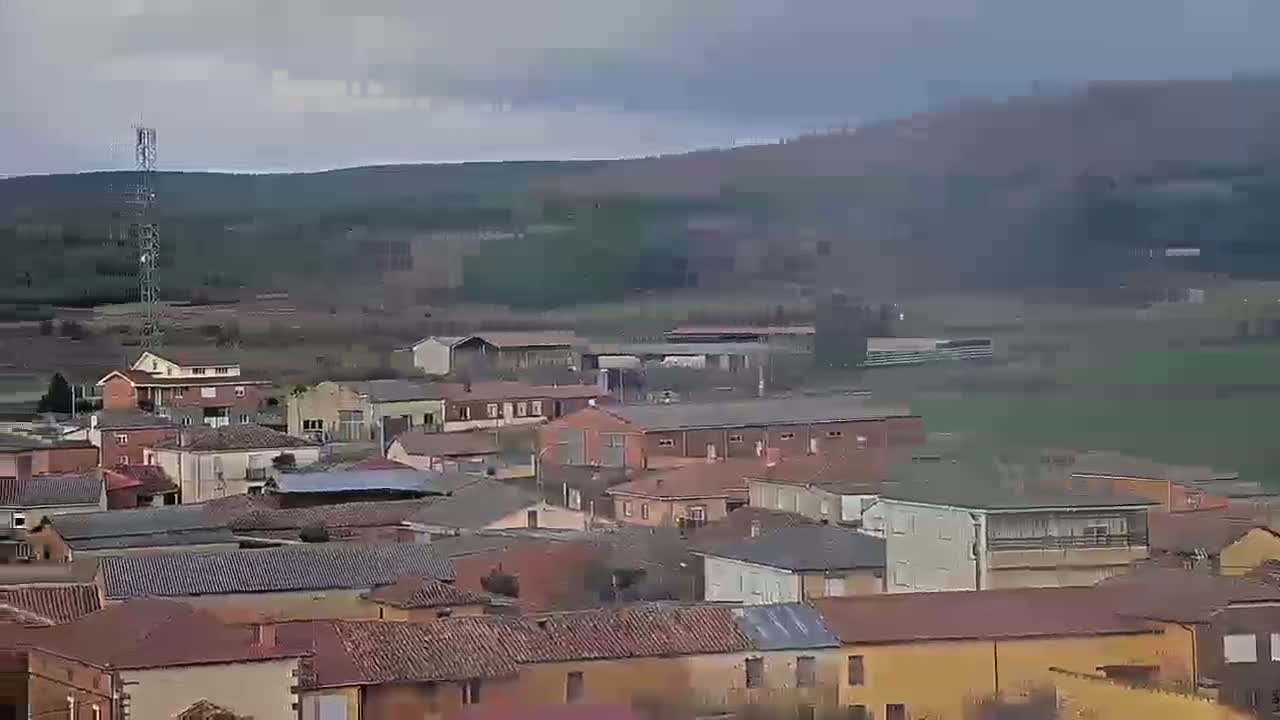 A small town with red-tiled roofs nestled in a valley under an overcast sky.