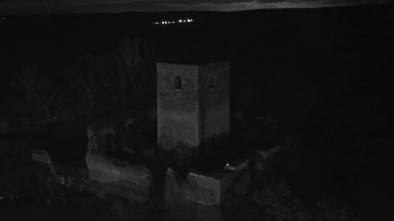 A dark gray stone tower is partially visible at night, with faint lights in the distance.