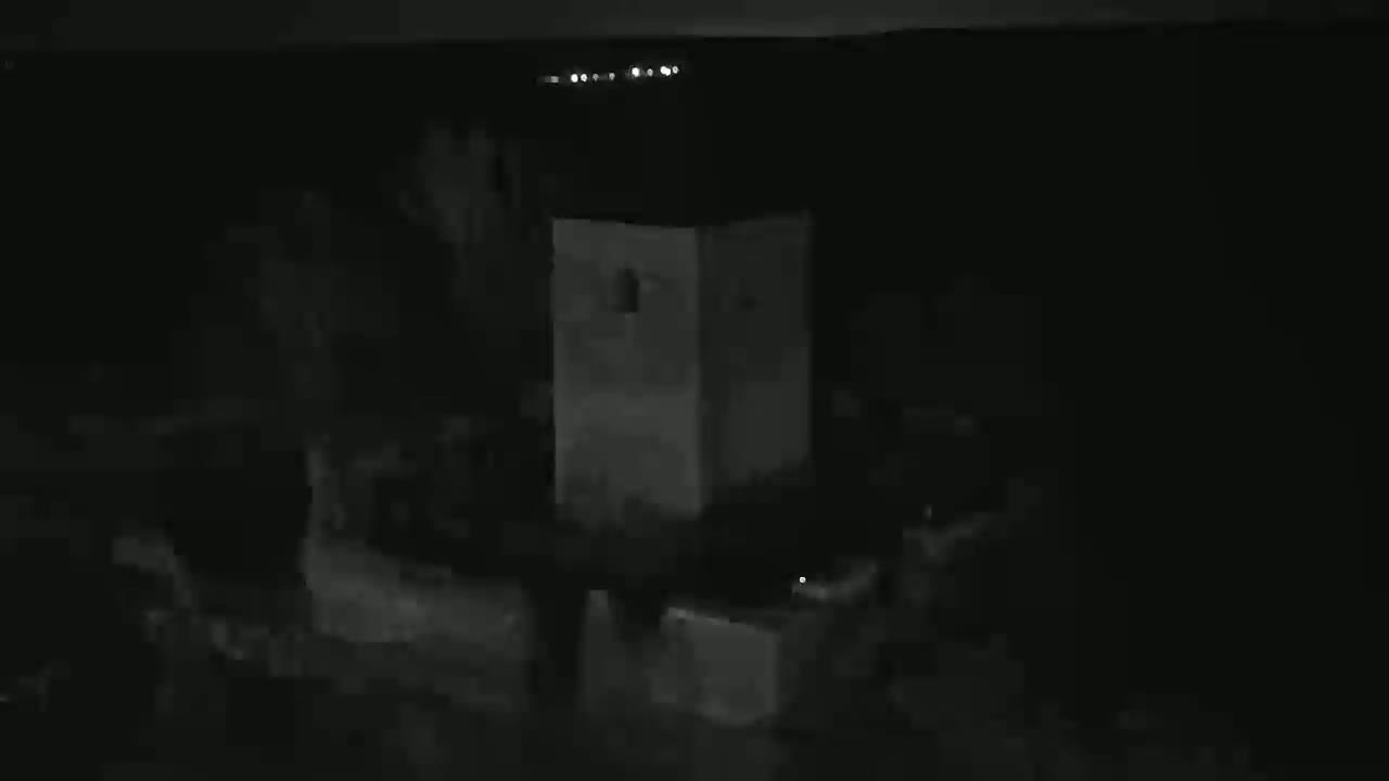 A blurry, nighttime image shows indistinct shapes near a light-colored, rectangular structure under a dark sky.