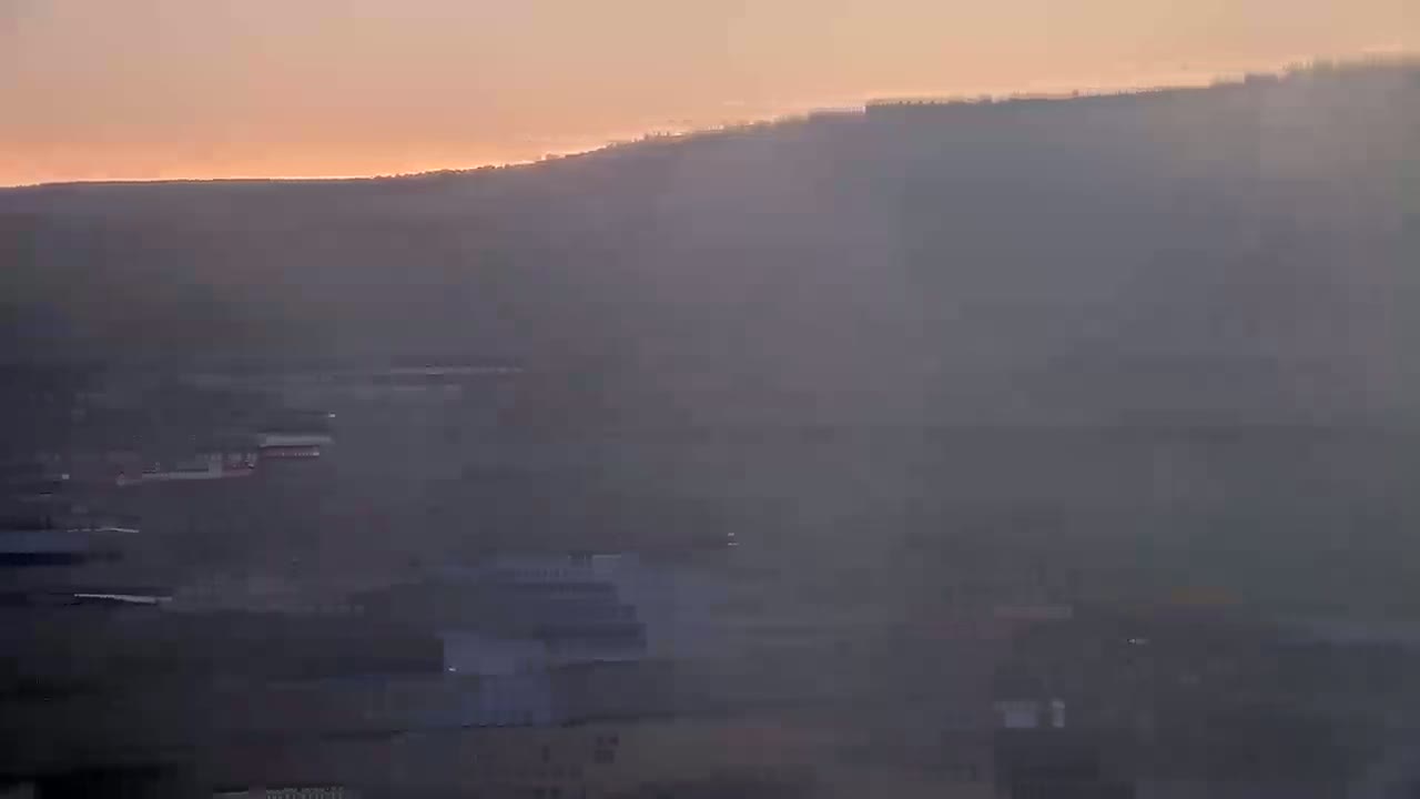 A hazy sunset illuminates a distant hill overlooking a blurry cityscape.