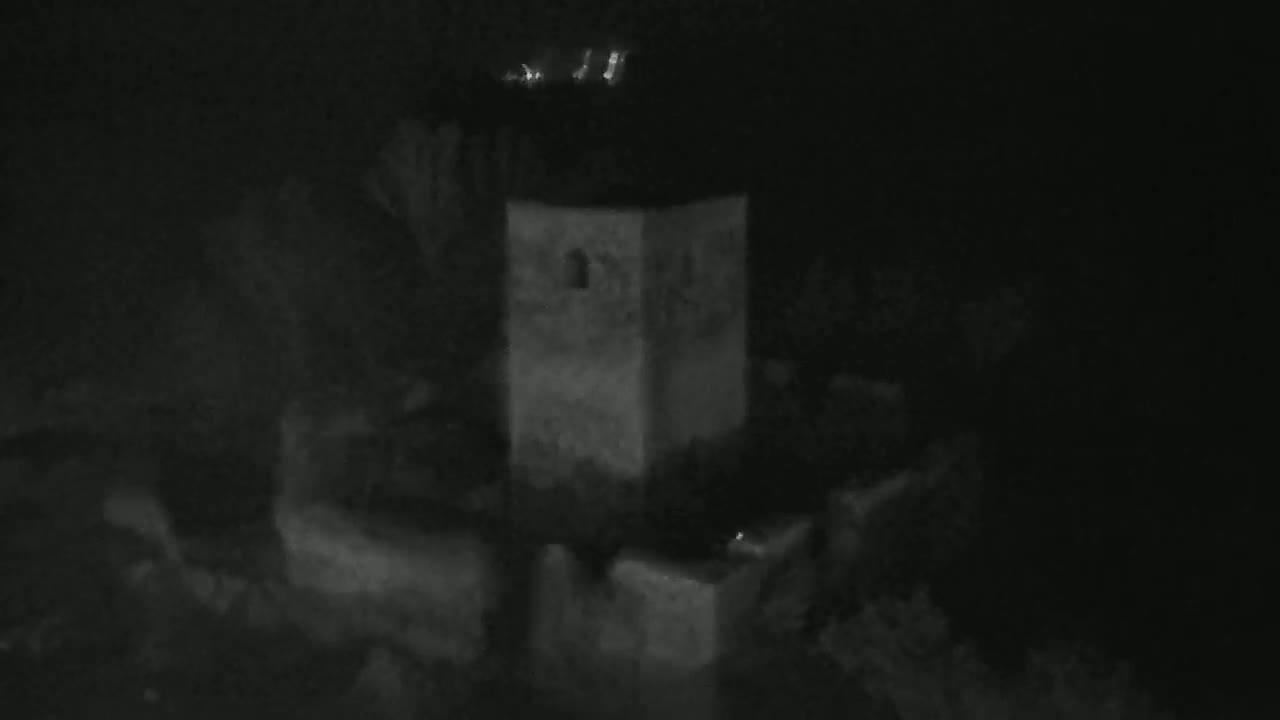 A blurry, gray structure resembling a tower is visible at night, partially obscured by darkness.