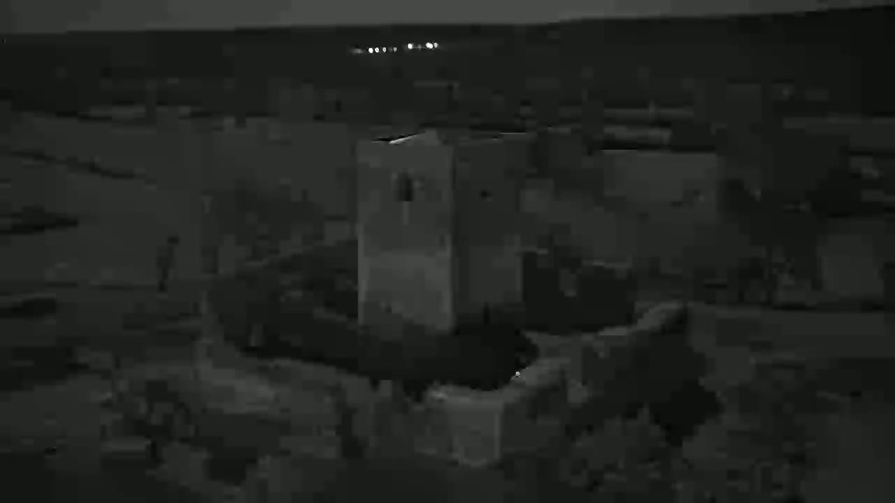 A nighttime, low-light aerial view shows a cluster of low buildings and structures.