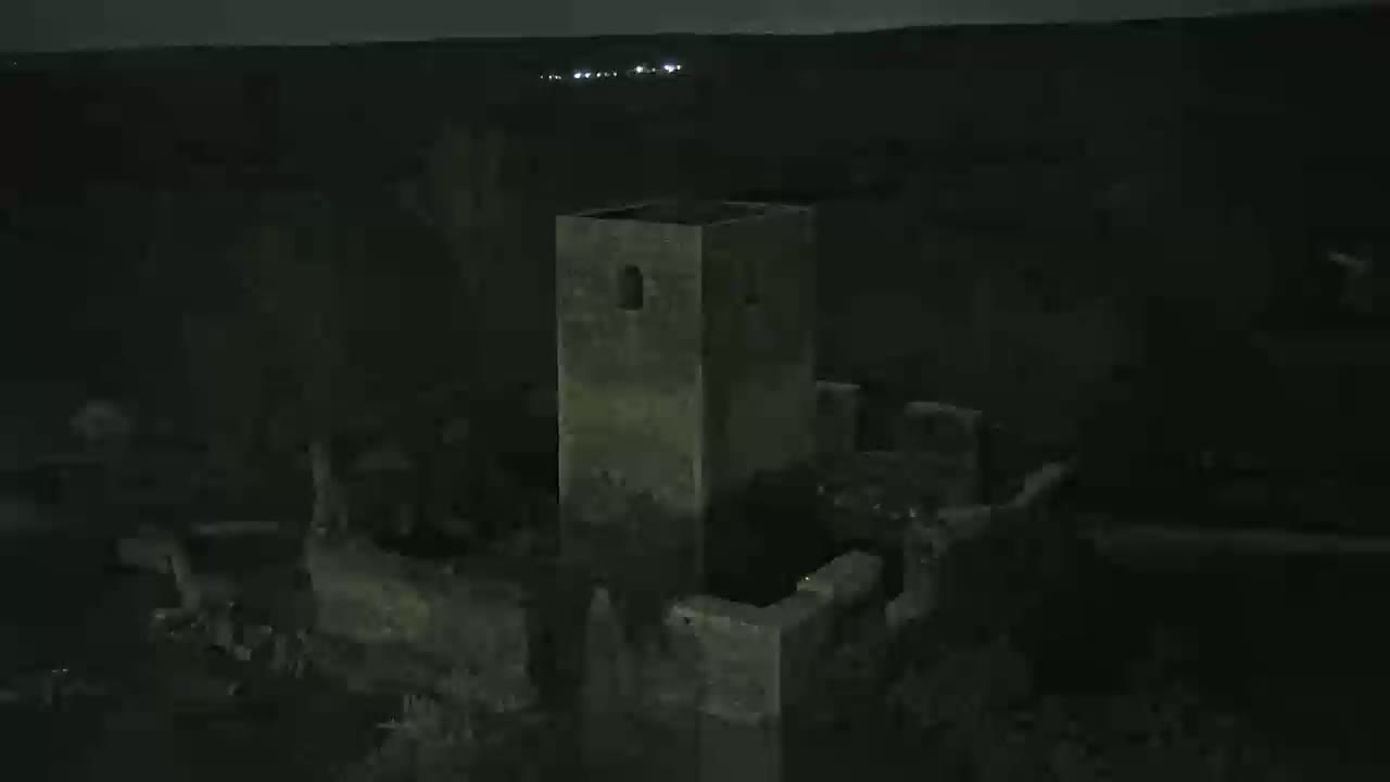 A nighttime aerial view shows the ruins of a stone structure, possibly a tower or castle, under a dark sky.