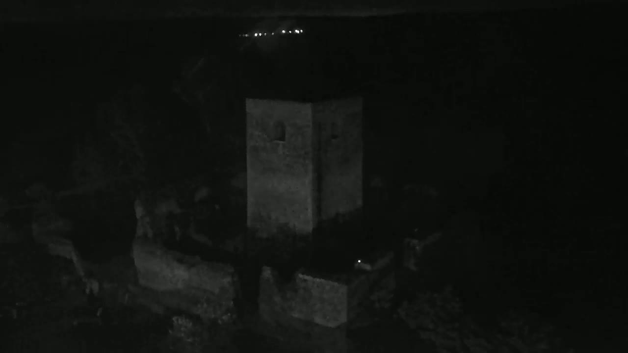 A stone tower and surrounding wall are visible at night under a dark sky with distant lights.