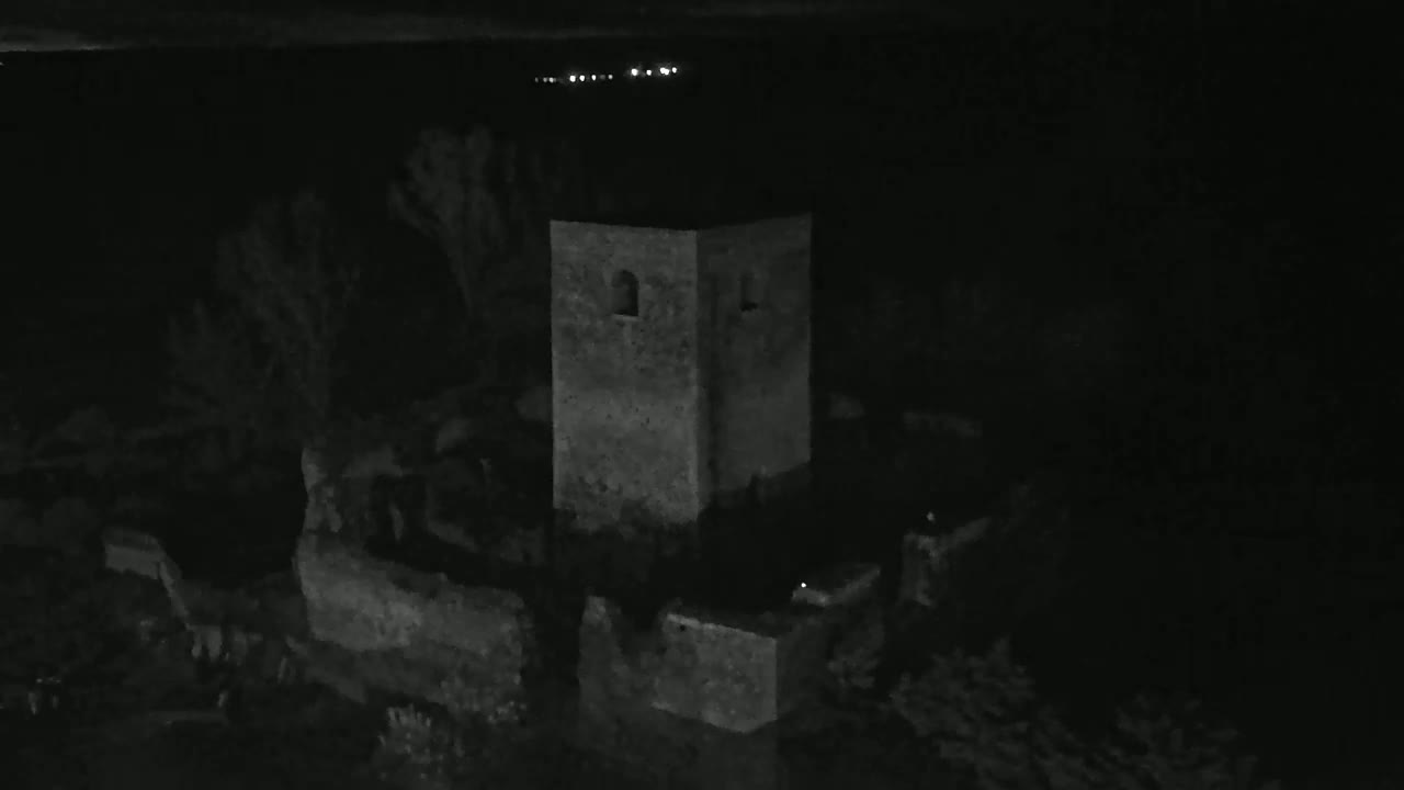 A stone tower and surrounding ruins are visible at night, under a dark sky with distant lights.