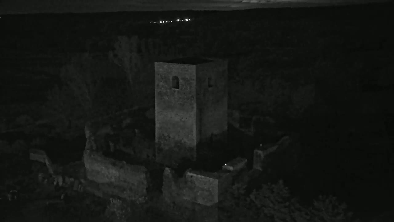 An aerial nighttime view shows the stone ruins of a castle, including a standing tower, under a dark sky.