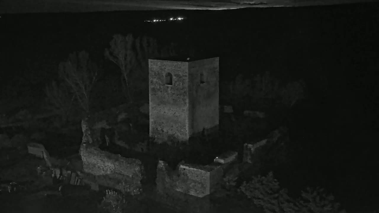 A stone tower, part of a larger ruined structure, stands in the dark of night amongst sparse vegetation under a clear sky.