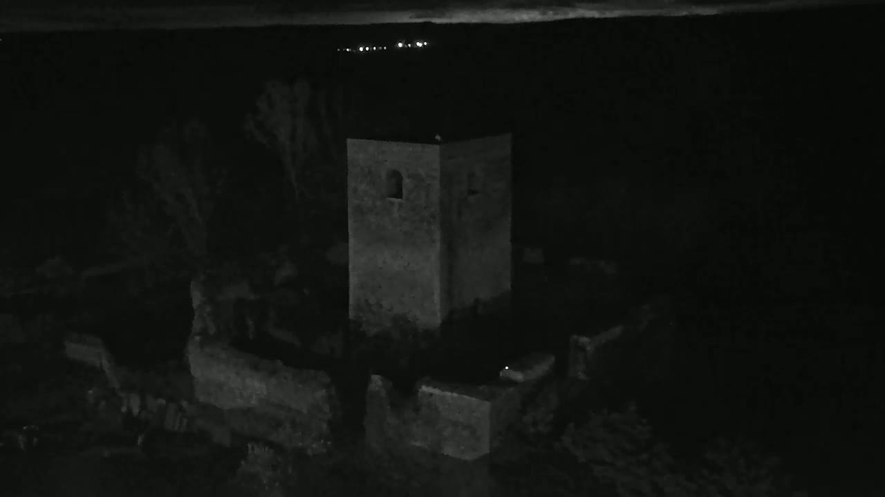 A stone tower and surrounding ruins are visible at night under a dark sky with distant lights.