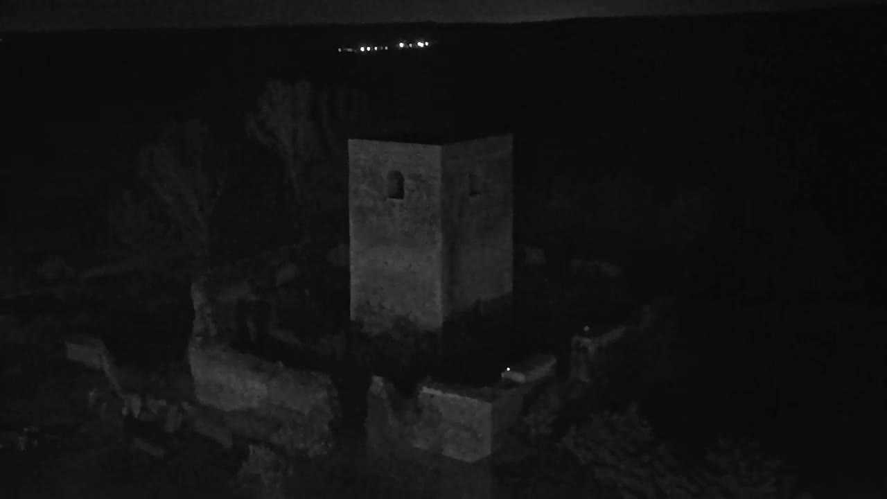A stone tower, partially surrounded by low walls, is visible at night under a dark sky with faint lights in the distance.