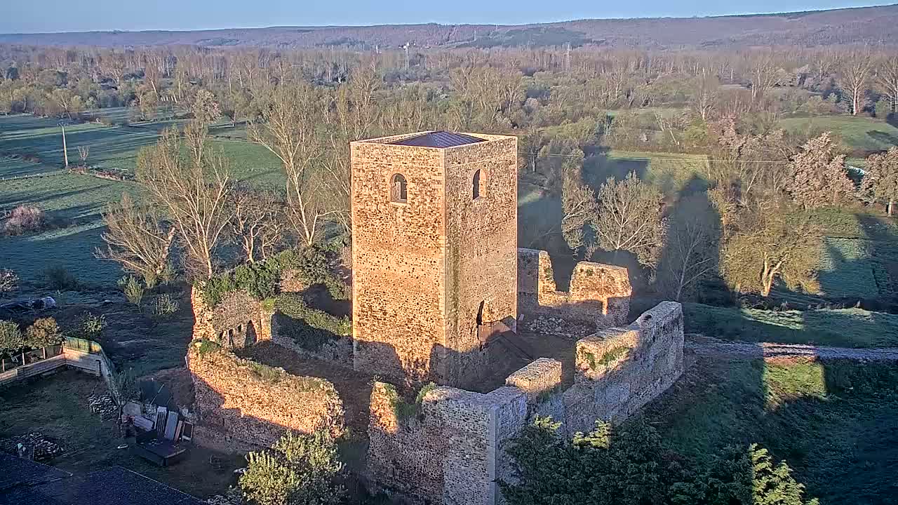 A stone tower and surrounding ruins are situated in a frost-covered landscape under a clear morning sky.