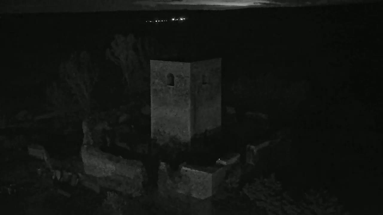 A stone tower, part of a larger ruin, is visible at night under a dark sky with faint lights in the distance.