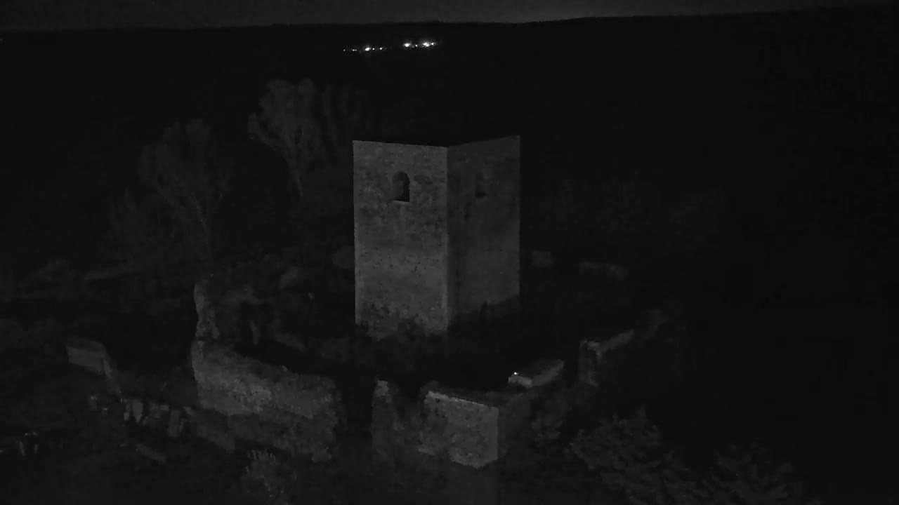 A stone tower and surrounding ruins are visible at night under dark, clear skies with distant lights in the background.
