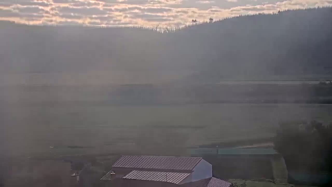 A hazy, dusty landscape shows a distant line of trees and hills under a pale sky, with a few buildings visible in the foreground.