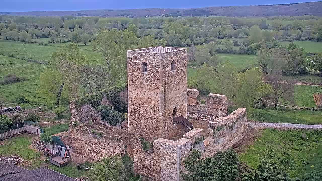 A stone tower and the ruins of a larger structure stand in a verdant valley under a partly cloudy sky.
