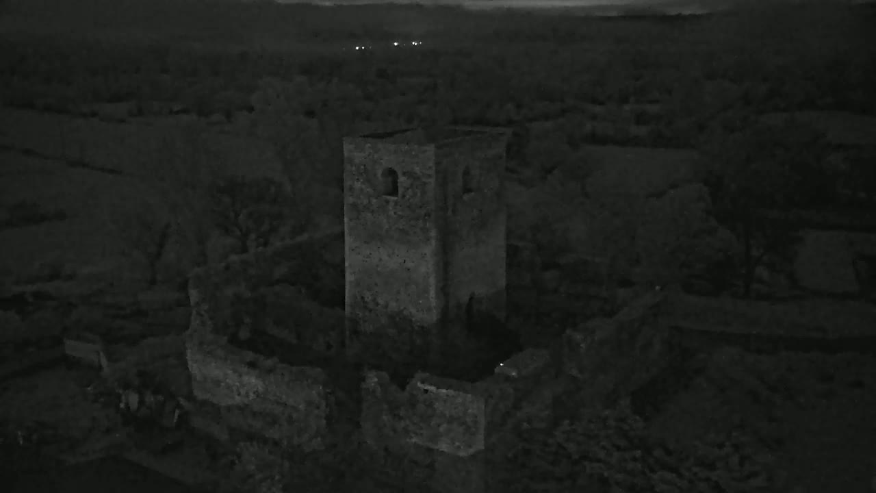 An aerial nighttime view shows the stone ruins of a tower and surrounding structures in a dark, rural landscape.