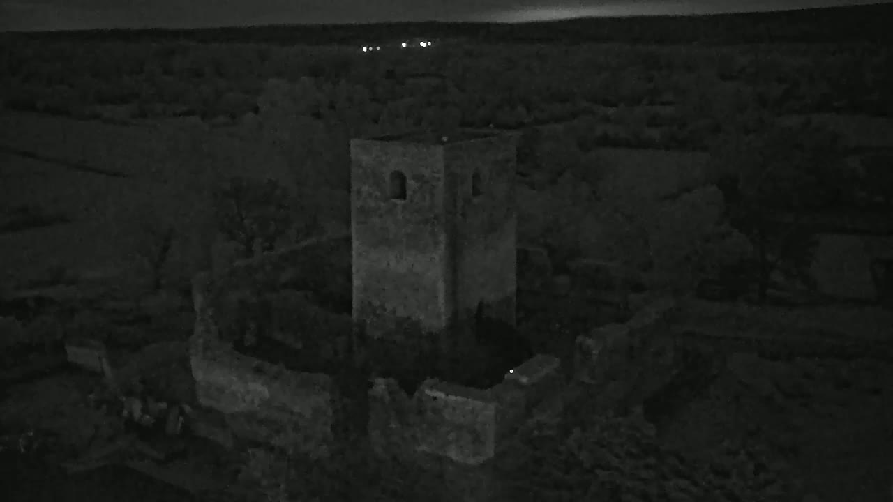 An aerial nighttime view shows the stone ruins of a tower and surrounding structures, under a dark sky.