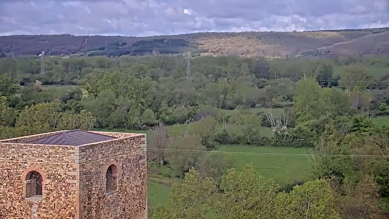 A stone tower with a flat roof overlooks a verdant valley under a partly cloudy sky.