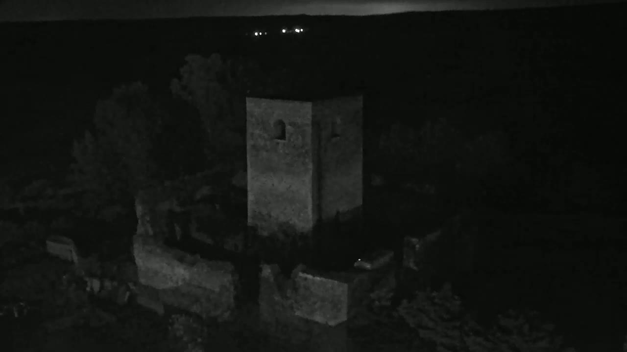 A stone tower and surrounding ruins are visible at night under a dark sky with distant lights.