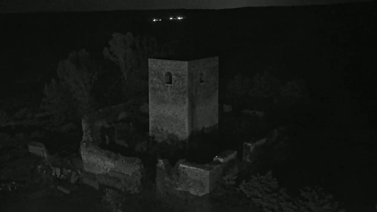 Stone ruins, including a standing tower, are partially visible at night under a dark sky with distant lights.