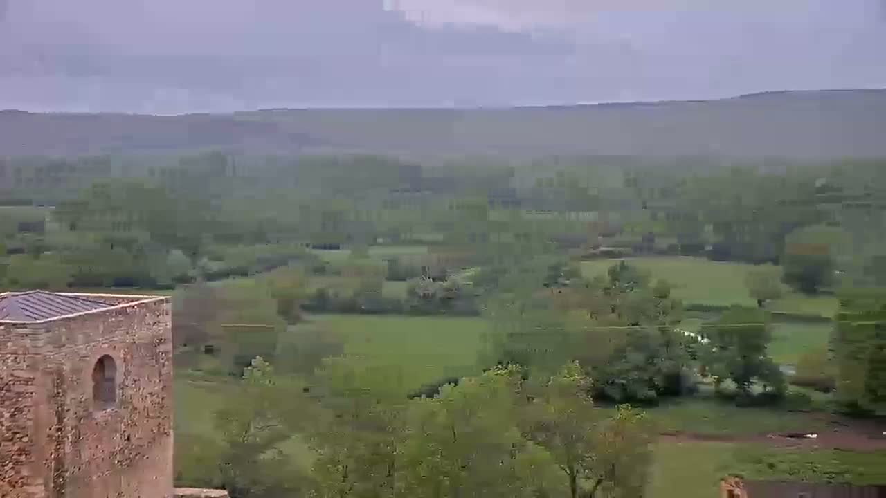 A stone structure with a small window overlooks a hazy, green valley under an overcast sky.