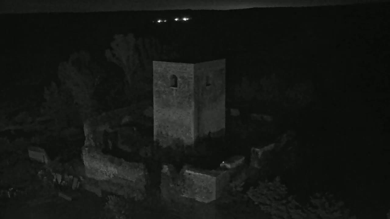 A stone tower and surrounding ruins are visible at night, under a dark sky with distant lights.