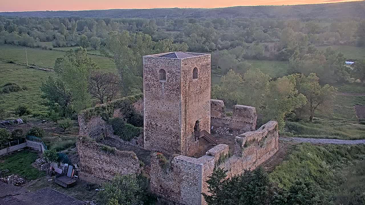 Stone ruins of a tower and castle walls sit on a hill overlooking a green valley at sunset.