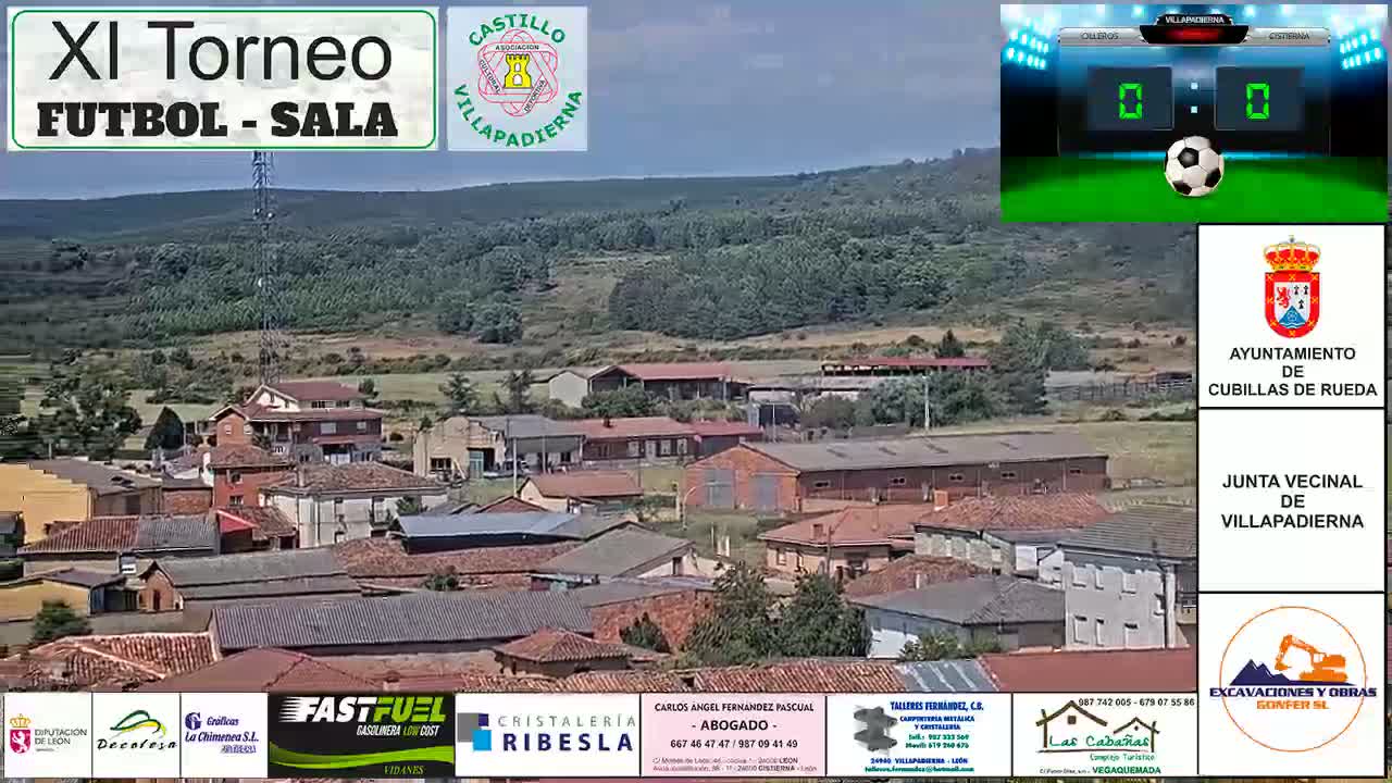 A sunny, daytime view of a small town nestled amongst green hills, featuring many brown-roofed buildings.