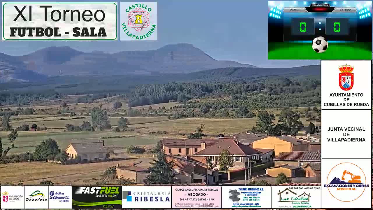 A sunny day reveals a rural town nestled in a valley, with a mountain range in the background.