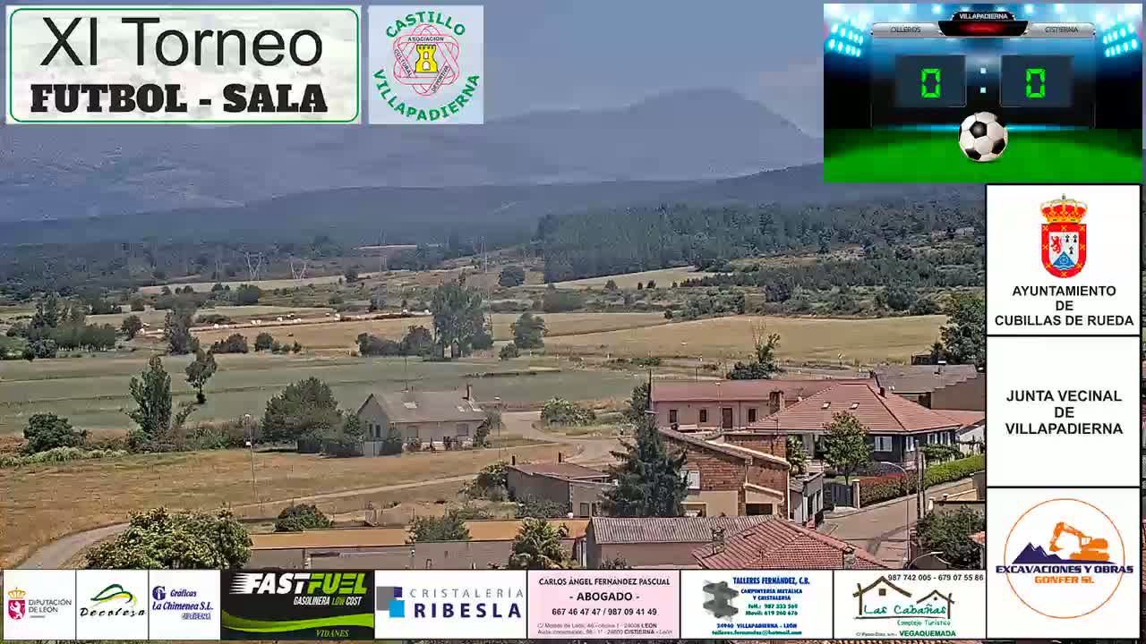 A sunny day overlooking a rural village nestled in a valley, with mountains in the background.