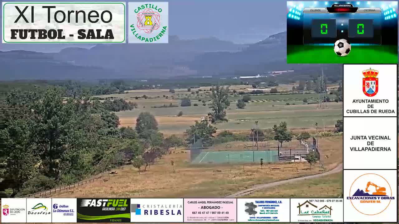A panoramic view of a rural area with green fields and trees under a hazy sky, showing a small, empty outdoor sports court in the foreground.