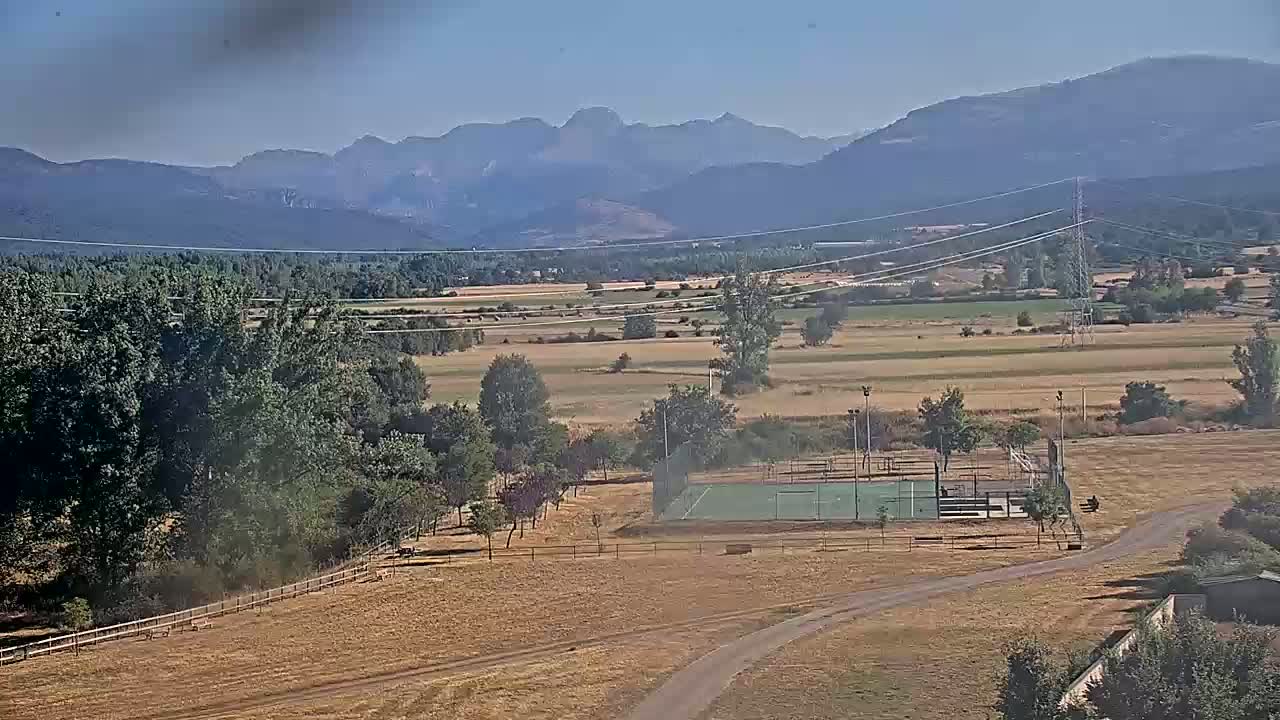 A small, green sports field is visible in the foreground of a dry, brown landscape, with a distant mountain range under a clear sky.