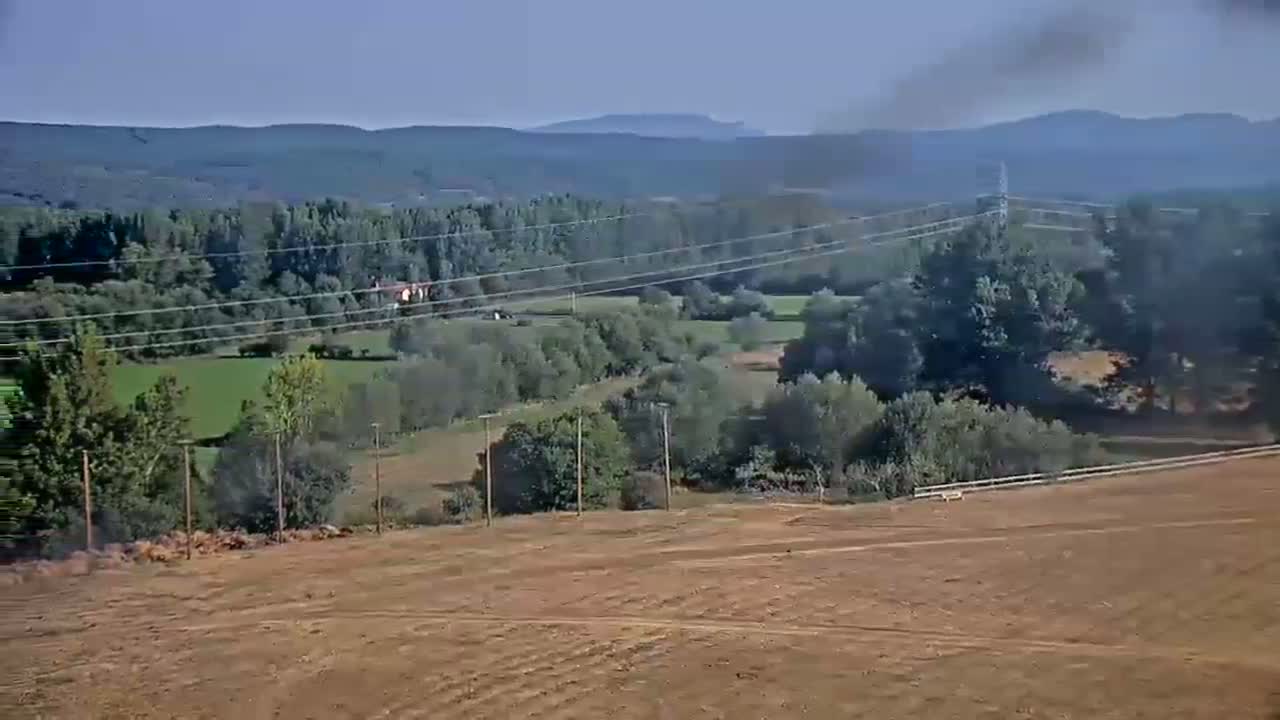 A hazy, sunny day reveals a rural landscape of brown fields, green trees and pastures, and distant mountains.