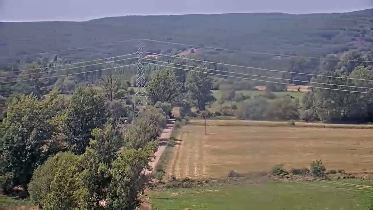 A hazy, sunny day reveals a rural landscape of brown fields, green trees and pastures, and distant mountains.