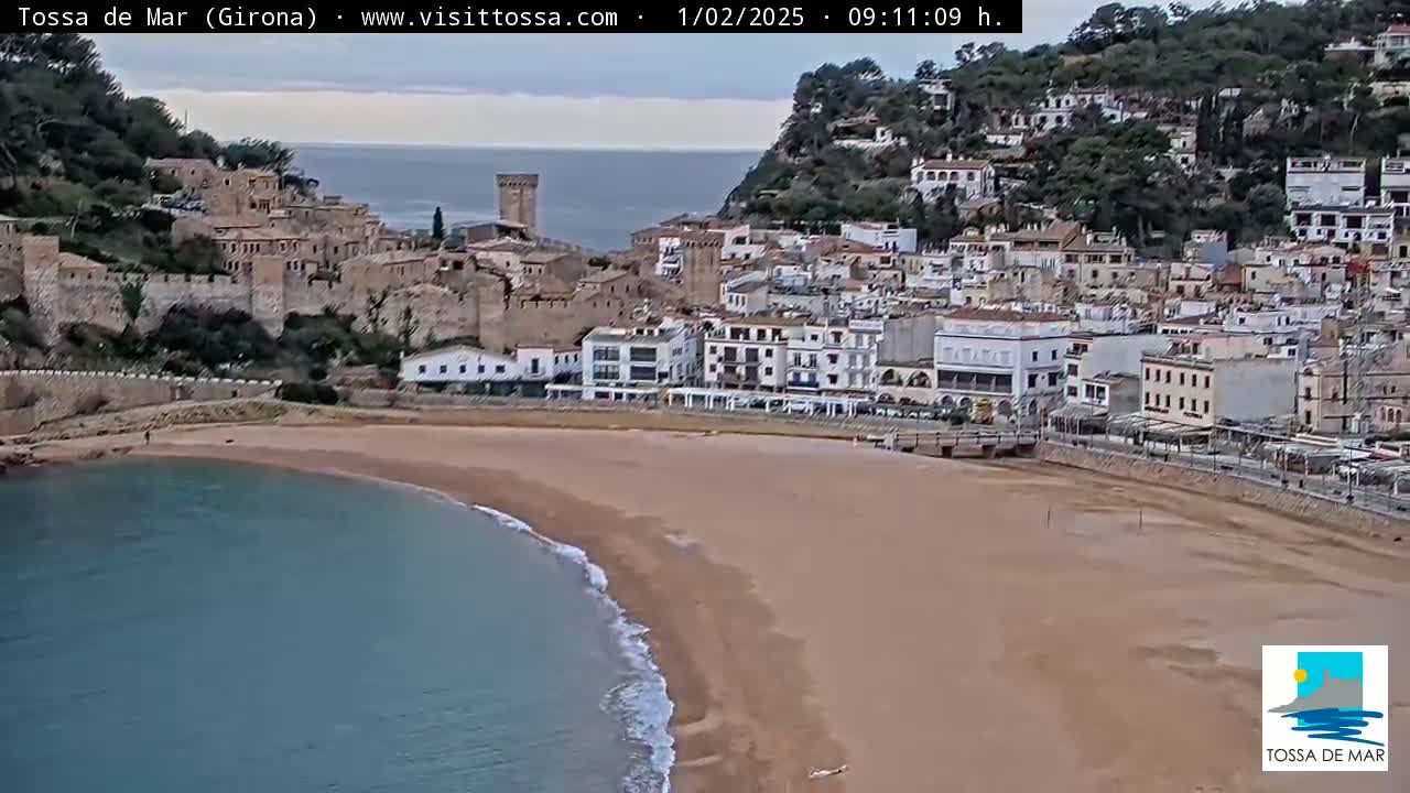 A coastal town with a sandy beach and calm sea under an overcast sky.