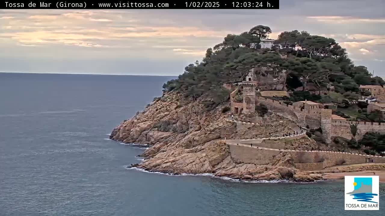 A rocky coastal cliff, topped with lush greenery and an old stone fortress, overlooks a calm sea under a partly cloudy sky.