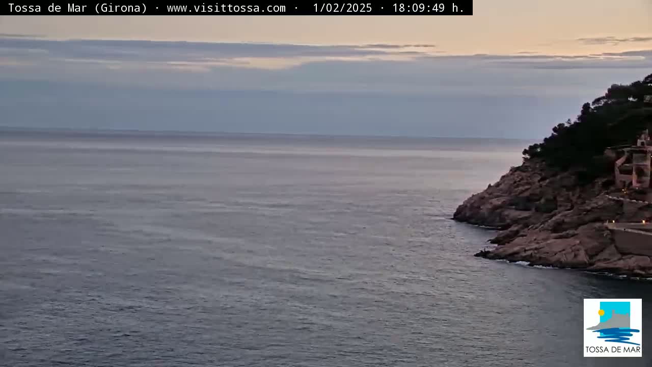 A calm sea meets a rocky shoreline under a partly cloudy evening sky.