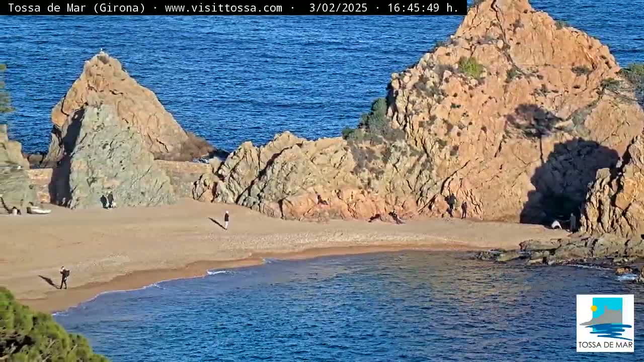 A sandy beach cove is nestled between two rocky outcrops, with a calm blue sea extending beyond.
