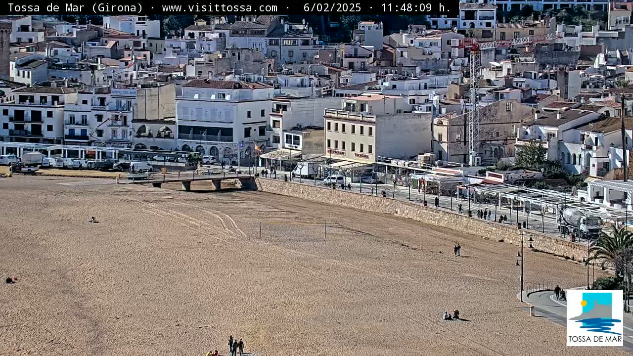 A sandy beach stretches below a coastal town of white buildings under a sunny sky.
