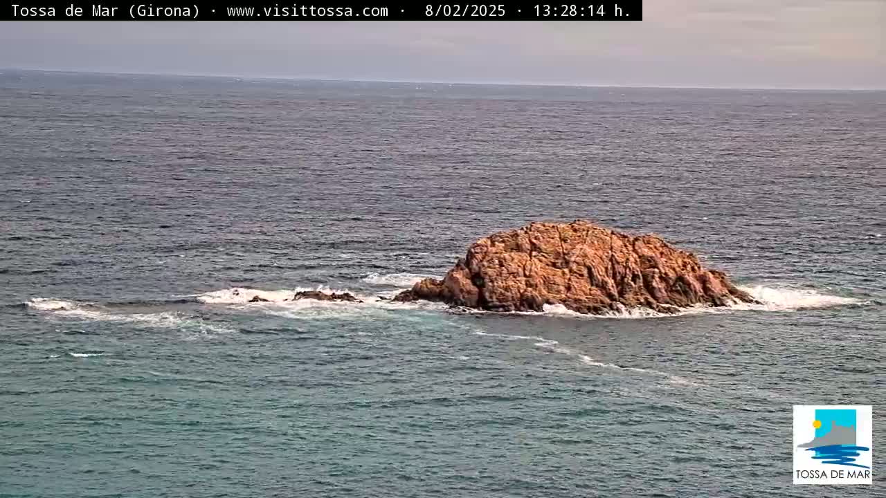 A small, rocky island sits in a calm sea under a mostly cloudy sky.